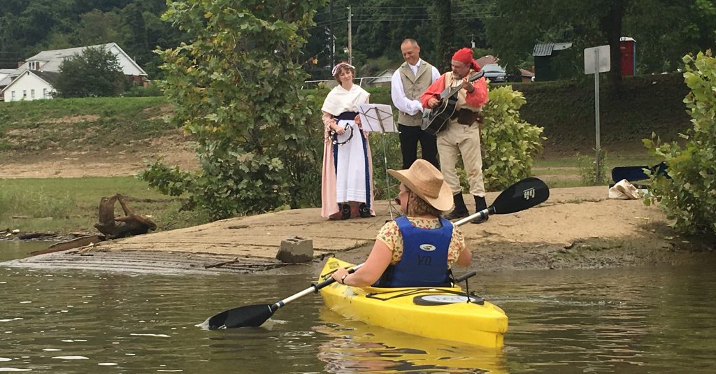 Musicians in period costume from the 1790s serenade a person kayaking down the river